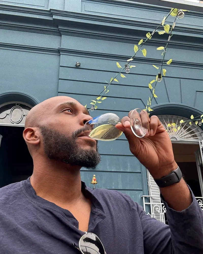Manuel Patterson sipping a glass of white wine in front of a blue building in Buenos Aires