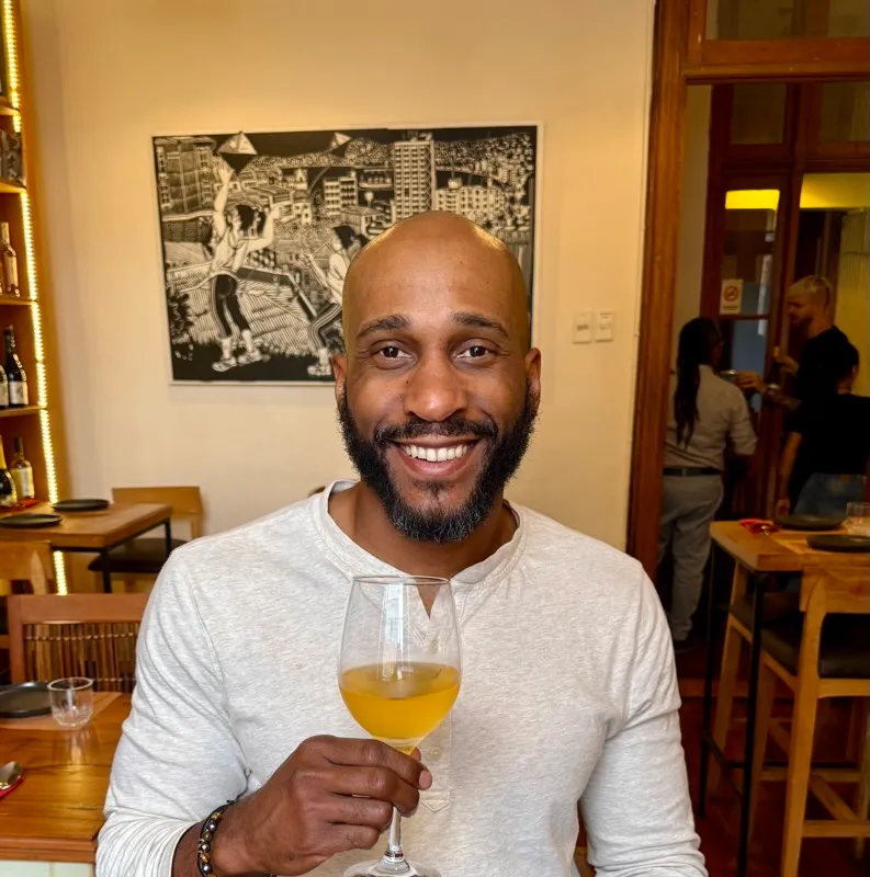 Manuel Patterson smiling and holding a glass of orange wine at a restaurant table