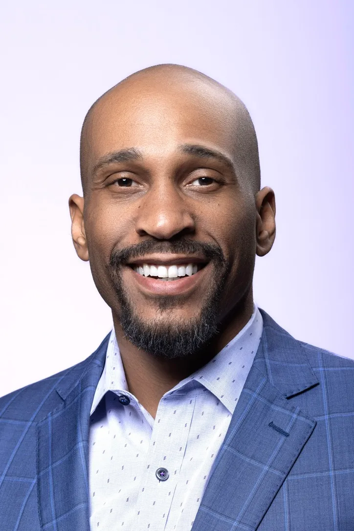 Portrait of Manuel Patterson, smiling, in a blue checked blazer