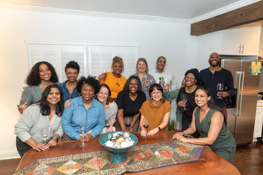 A group of smiling guests holding wine glasses posing around a table with Manuel Patterson