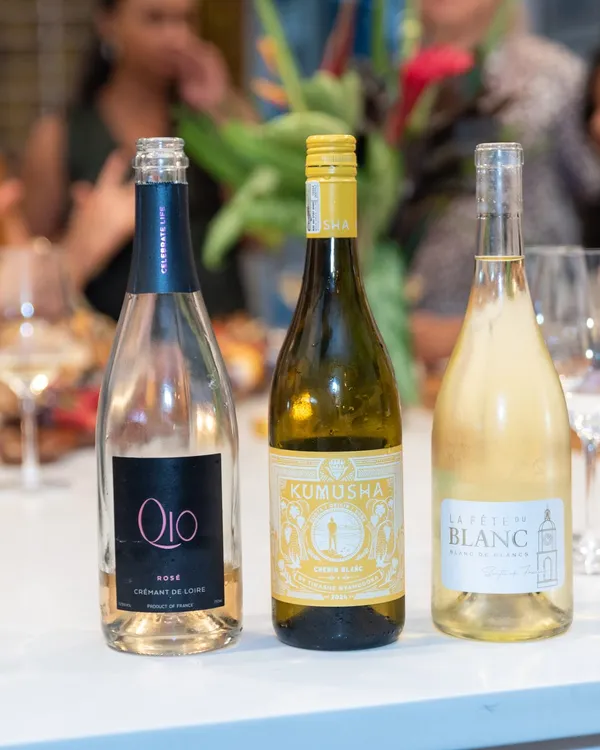 A rosé, a white and a blanc de blancs standing on a kitchen island with guests chatting behind