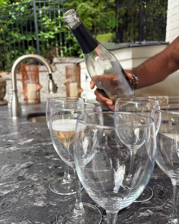 A bottle of sparkling wine being poured into glasses on a granite counter