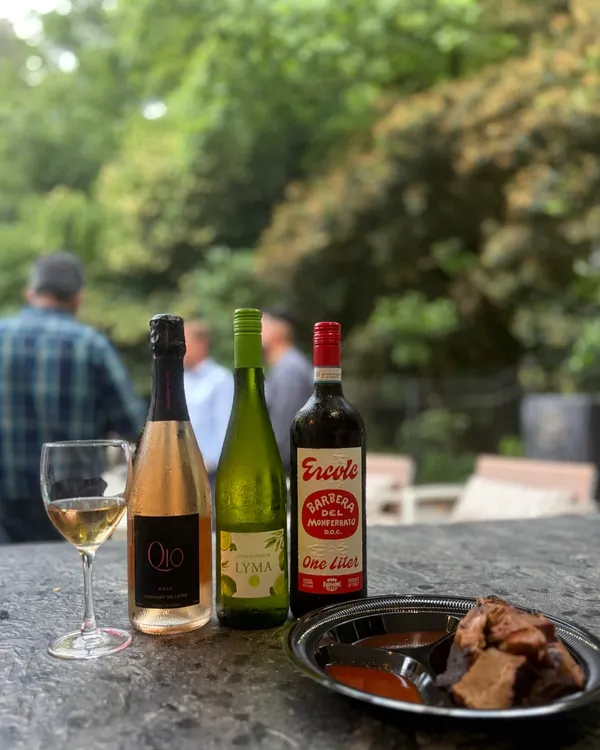 Three bottles of wine lined up on a stone counter with a glass of white wine and a snack plate
