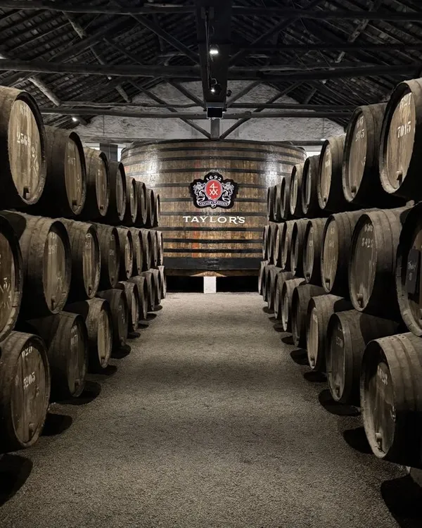 A long aisle between stacked wooden port barrels leading to a giant cask with a Taylor's logo